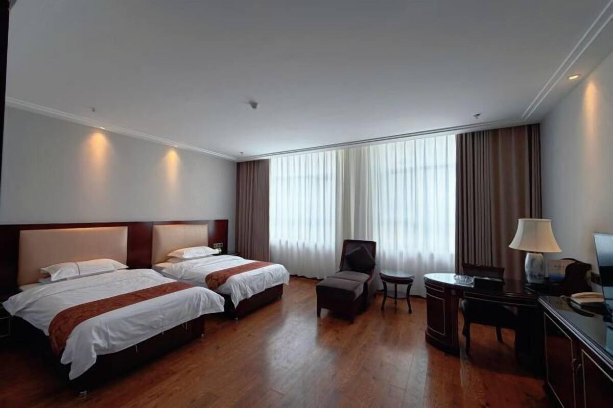 A hotel room with two beds, a desk, a chair, a lamp, and a TV.