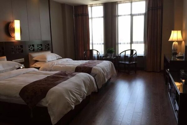 A hotel room with two beds, a desk, a chair, and large windows with curtains.