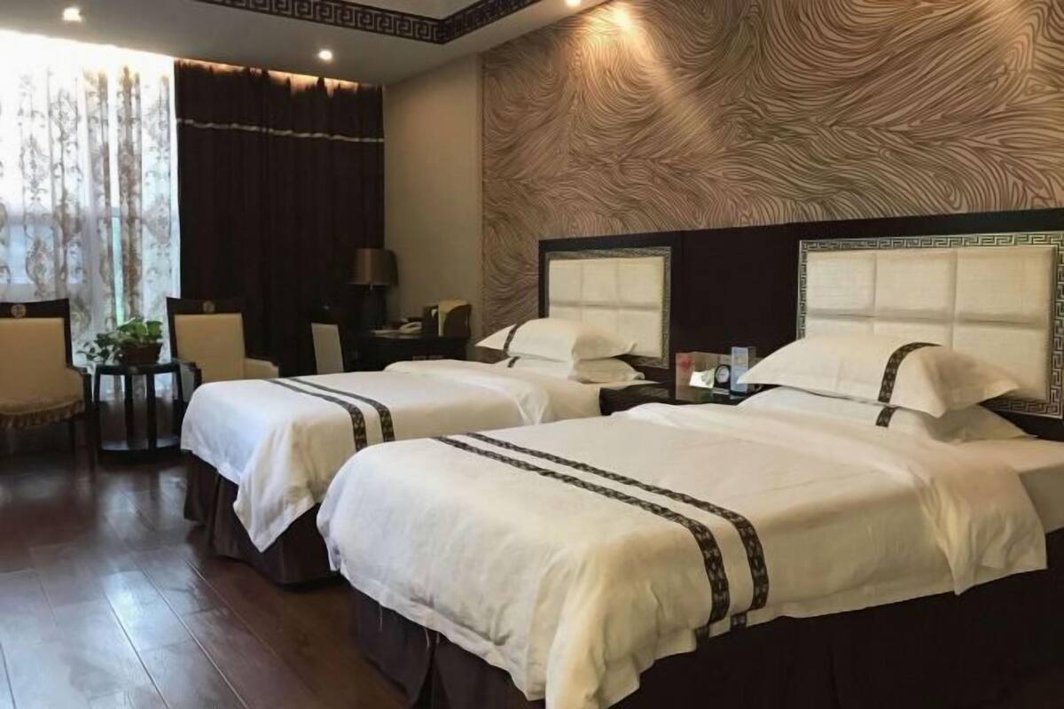 A hotel room with two beds, a desk, a chair, and a large window with curtains.