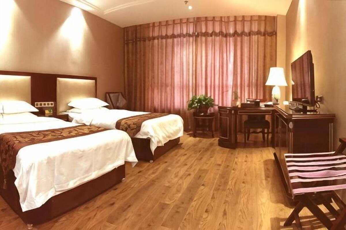 A hotel room with two beds, a desk, a chair, a lamp, and a television.