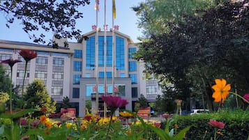 A building with a central entrance, surrounded by a garden with various flowers.