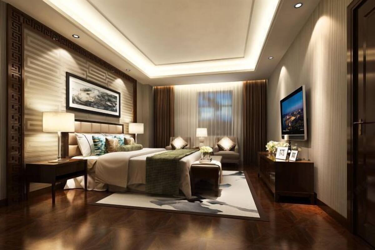 A modern hotel room with a large bed, bedside tables, a flat-screen TV, and a view of the city through large windows.