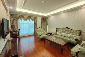 A spacious living room with a large sofa, a coffee table, and a television on a stand. - Manas County Hotel (Manas County)