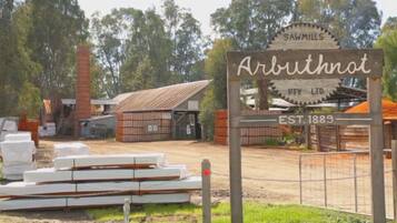 Un letrero de 'Arbuthtnot Sawmills Pty Ltd' con una estructura de madera rústica y una chimenea de ladrillo al fondo.