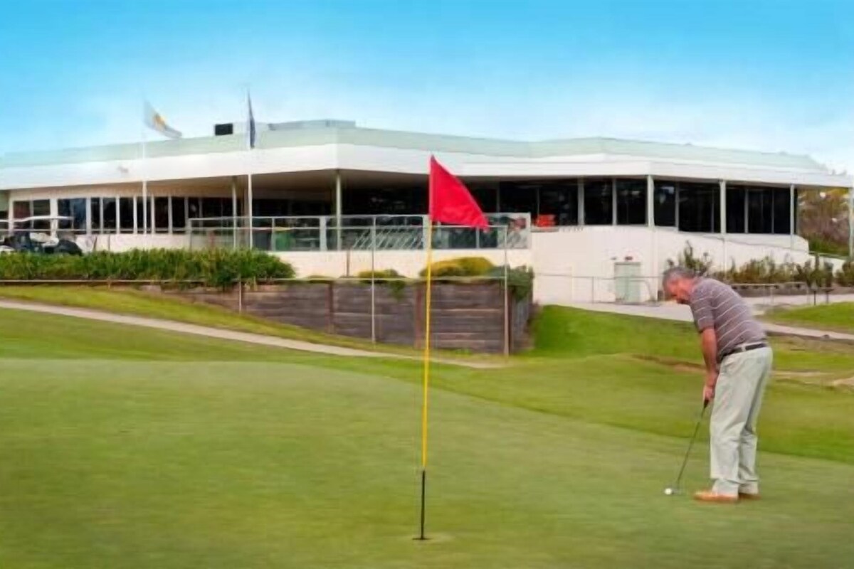 A golf course with a flagstick, a building with large windows, and a clear sky.