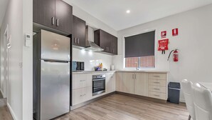 Eine moderne Küche mit Edelstahlkühlschrank, Holzschränken, einem eingebauten Ofen und einem Fenster mit Jalousien.