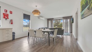 Ein modernes Wohnzimmer mit Essbereich, einem großen Fenster mit Vorhängen, einem Feuerlöscher und einer Deckenleuchte.