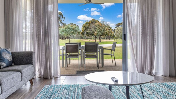 Ein Wohnzimmer mit grauem Sofa, einem runden Couchtisch und Blick auf eine Terrasse mit Tisch und Stühlen.