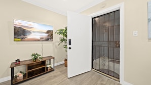 Una habitación con una consola de madera, una planta en maceta, una puerta con reja metálica y un cuadro en la pared.