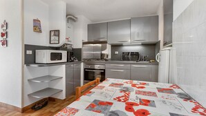 A compact kitchen with a microwave, coffee maker, and a small oven. There is a wooden chair and a table with a pop art tablecloth. - Spacious Apt 7 ppl, terrace, near the sea (Agde)