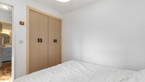 A bedroom with a bed, a wooden wardrobe, and a bathroom visible through an open door. - Spacious Apt 7 ppl, terrace, near the sea (Agde)