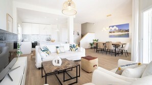 Un salon moderne avec un canapé blanc, une table basse et un coin repas comprenant une table et des chaises en bois.