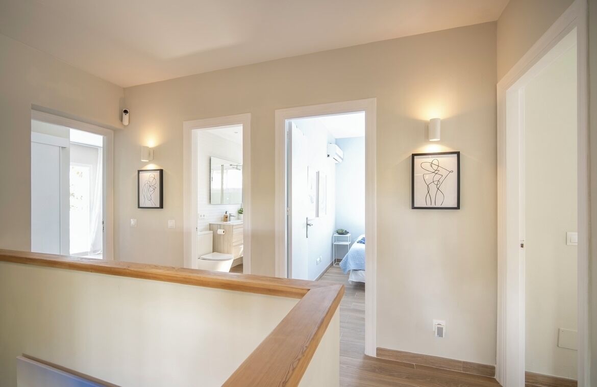 A modern hallway with a wooden railing, light-colored walls, and framed artwork.