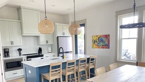 Una cucina moderna con mobili bianchi, una grande isola con sgabelli da bar, un tavolo da pranzo e un'opera d'arte colorata al muro.