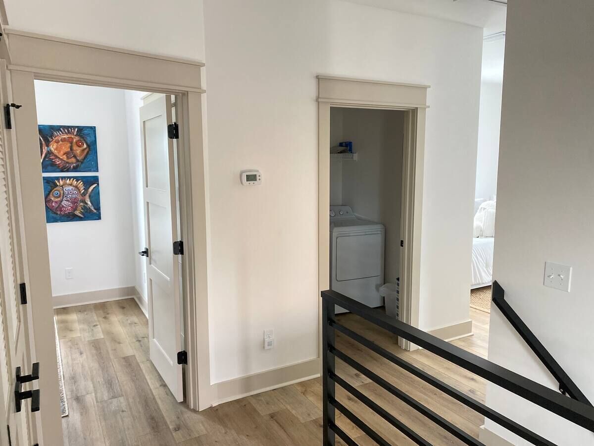 Een modern appartement met een houten vloer, een trap met zwarte leuningen, en een wasruimte met een wasmachine.