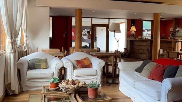 Uma sala de estar acolhedora e rústica, com piso de madeira, móveis brancos e uma mesa de centro com objetos decorativos.