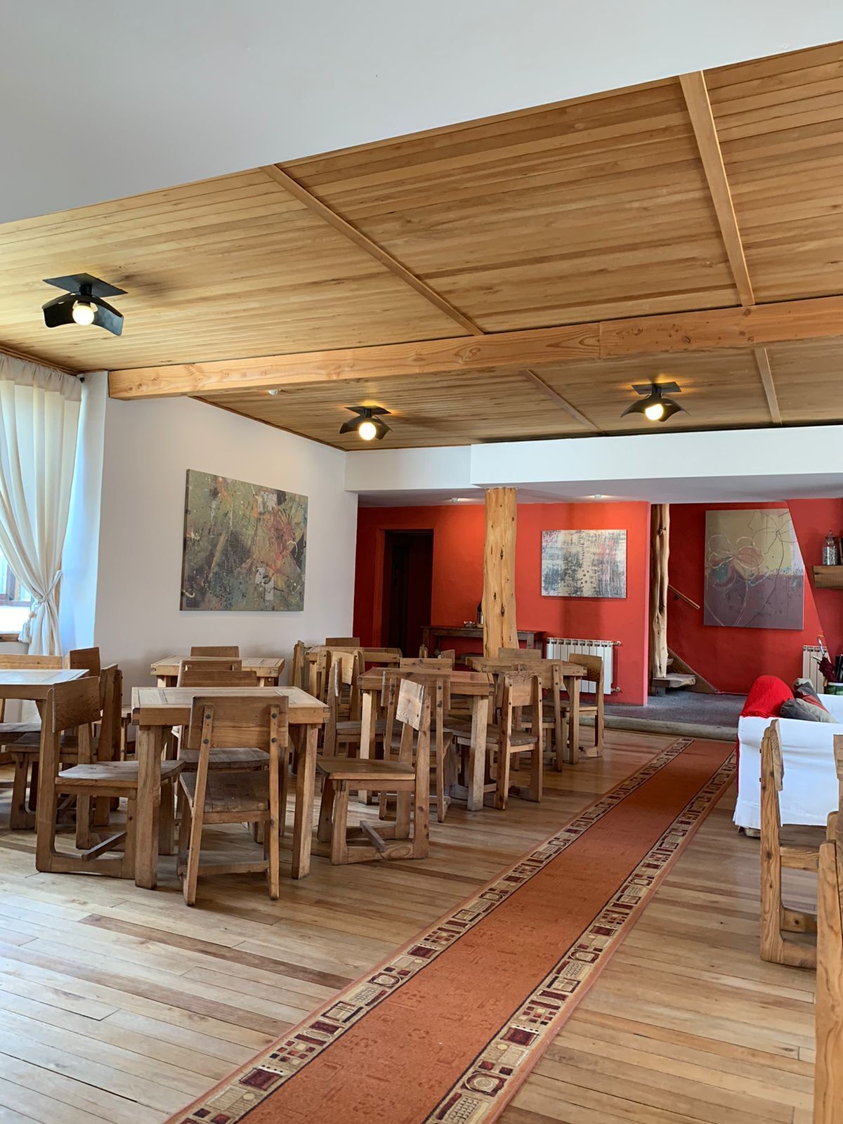 A dining area with wooden tables and chairs, a red carpet, and ceiling fans.
