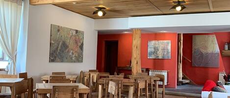 A dining area with wooden tables and chairs, a red carpet, and ceiling fans.