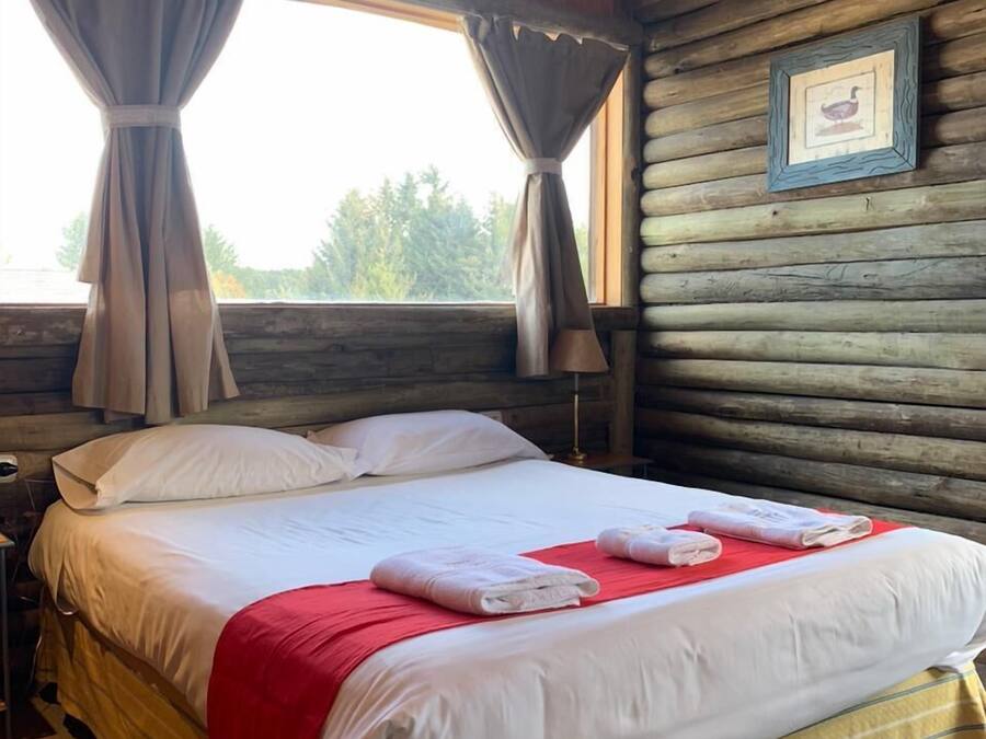 A wooden cabin room with a bed, curtains, a framed picture, and a window.
