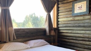 Quarto de cabana de madeira com cama, cortinas e um quadro na parede.