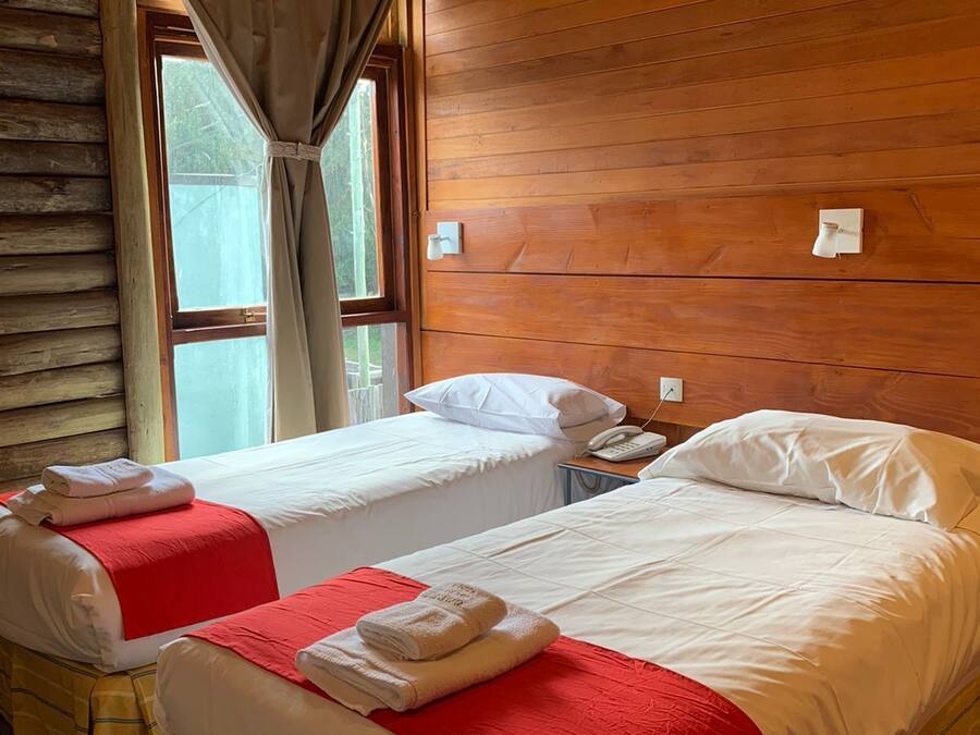Una habitación con dos camas, paredes de madera, una ventana con cortinas y una mesita de noche con un teléfono.