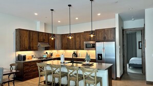 A modern kitchen with wooden cabinets, a central island with bar stools, stainless steel appliances, and pendant lighting. - New, modern mountain retreat for several families 8 min from ski resort. (Fraser)