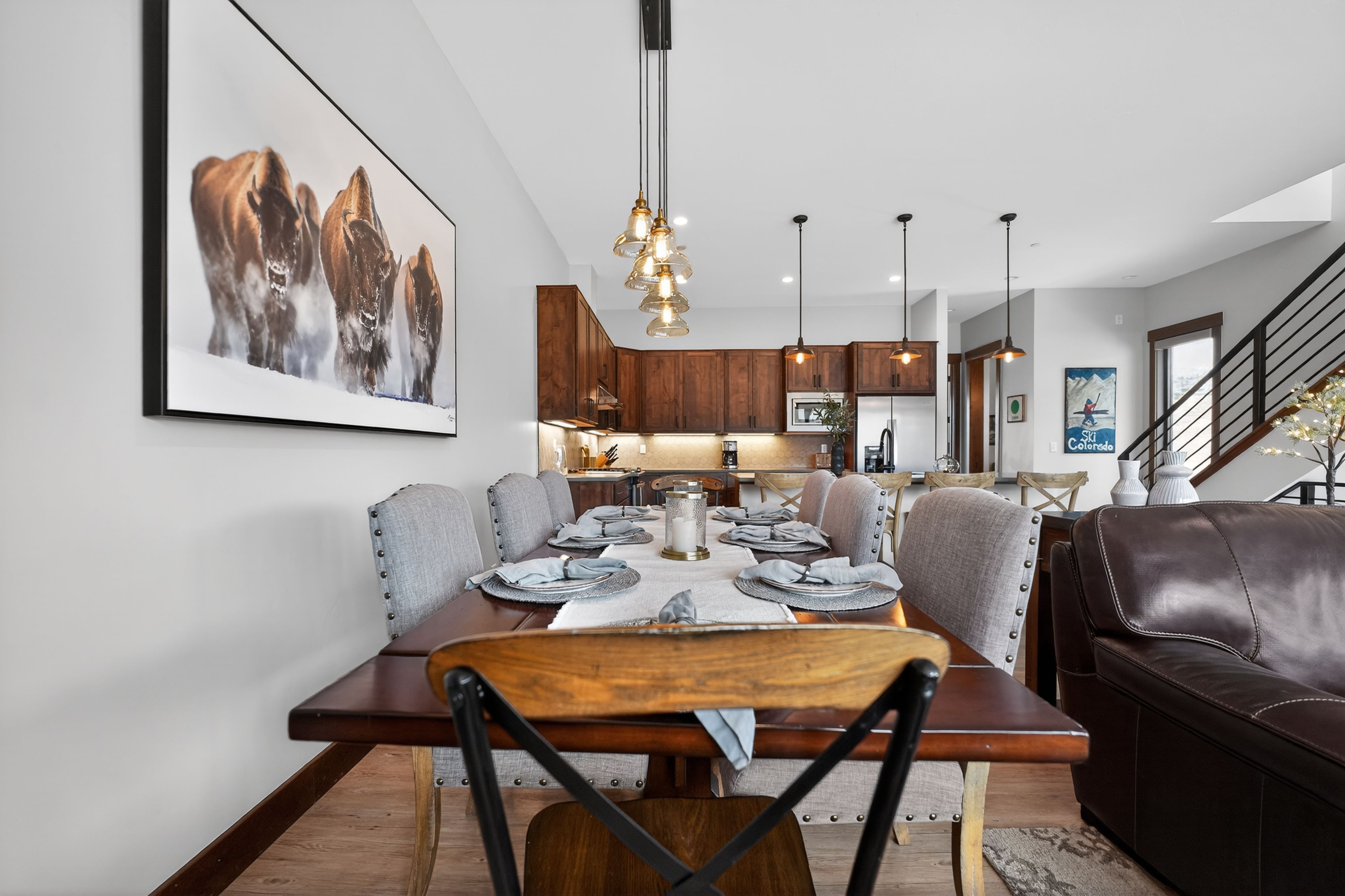 A modern dining area with a wooden table set for four, surrounded by grey upholstered chairs.