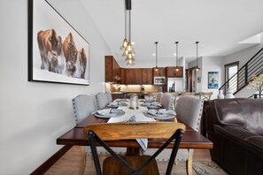 Un espace repas moderne avec une table en bois, dressée pour quatre personnes, entourée de chaises à revêtement gris.