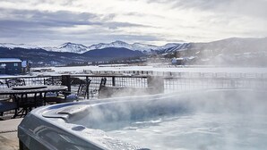 A hot tub with steam rising, surrounded by a metal fence, overlooking a snowy landscape with mountains and a body of water. - New, modern mountain retreat for several families 8 min from ski resort. (Fraser)