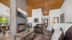 A cozy living room with a fireplace, leather sofa, and a dining area with wooden furniture. - Modern, Cozy with Stunning Mountain View, Hot Tub, Arcade, Mins to the Smokies (Seiverville)