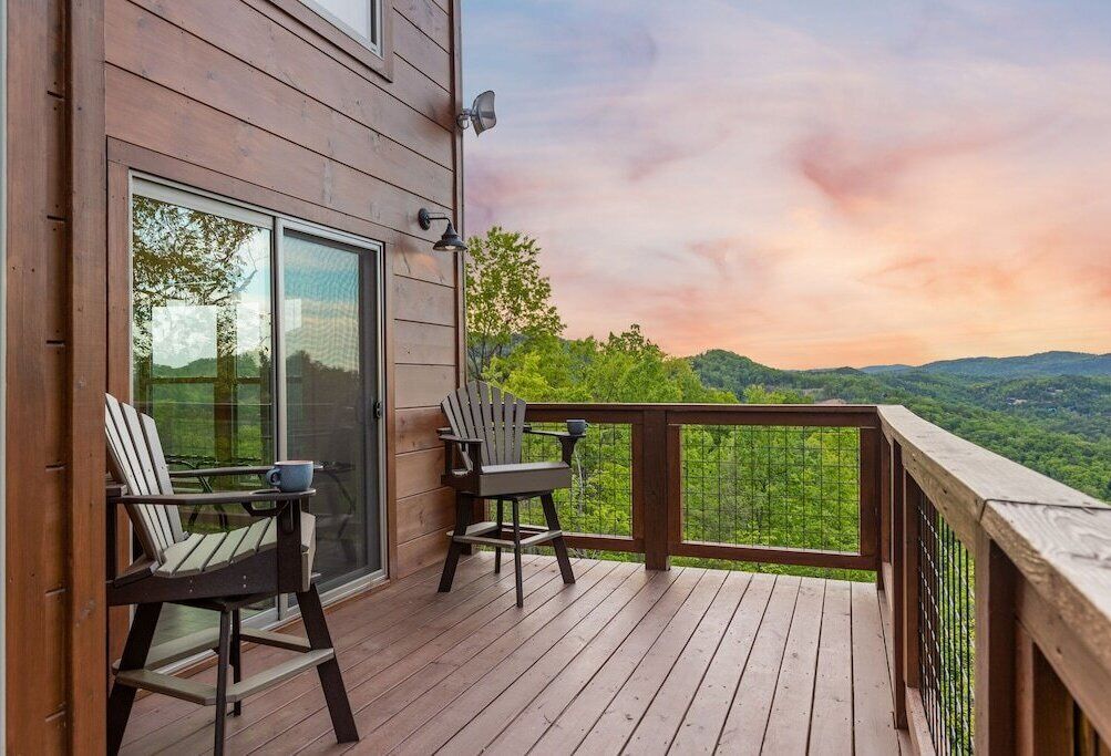 Una terraza de madera con dos sillas Adirondack y una mesa, con vistas a un paisaje verde y exuberante.