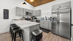 A modern kitchen with a central island, stainless steel appliances, and bar stools. - Modern, Cozy with Stunning Mountain View, Hot Tub, Arcade, Mins to the Smokies (Seiverville)