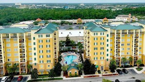 A multi-story hotel with a central swimming pool, surrounded by lush greenery and a parking area. - Close to Disney and Universal! Family-sized condo with pool, balcony & game room (Orlando)