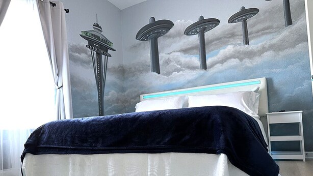 A bedroom with a bed, a nightstand, and a wall mural of the Space Needle and UFOs. - Close to Disney and Universal! Family-sized condo with pool, balcony & game room (Orlando)