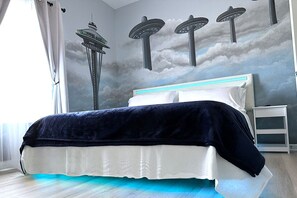 Quarto com cama, mesa de cabeceira e um mural na parede retratando a Space Needle e OVNIs.