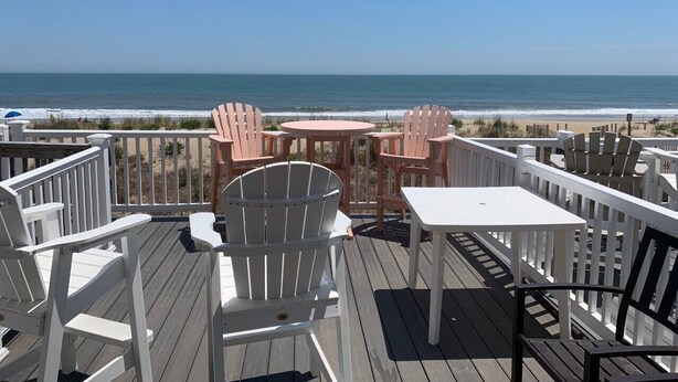 A deck with white and pink Adirondack chairs and a white table, overlooking a beach. - Extra large direct oceanfront townhouse. Sleeps 14. (Ocean City)