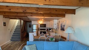 A living room with a blue sofa, wooden flooring, a staircase, and a kitchen area in the background. - Extra large direct oceanfront townhouse. Sleeps 14. (Ocean City)