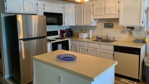 A compact kitchen with white cabinets, a stainless steel refrigerator, a microwave, a sink, and a dishwasher. - Extra large direct oceanfront townhouse. Sleeps 14. (Ocean City)