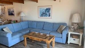 A living room with a blue sectional sofa, a wooden coffee table, and a white side table with a lamp. - Extra large direct oceanfront townhouse. Sleeps 14. (Ocean City)