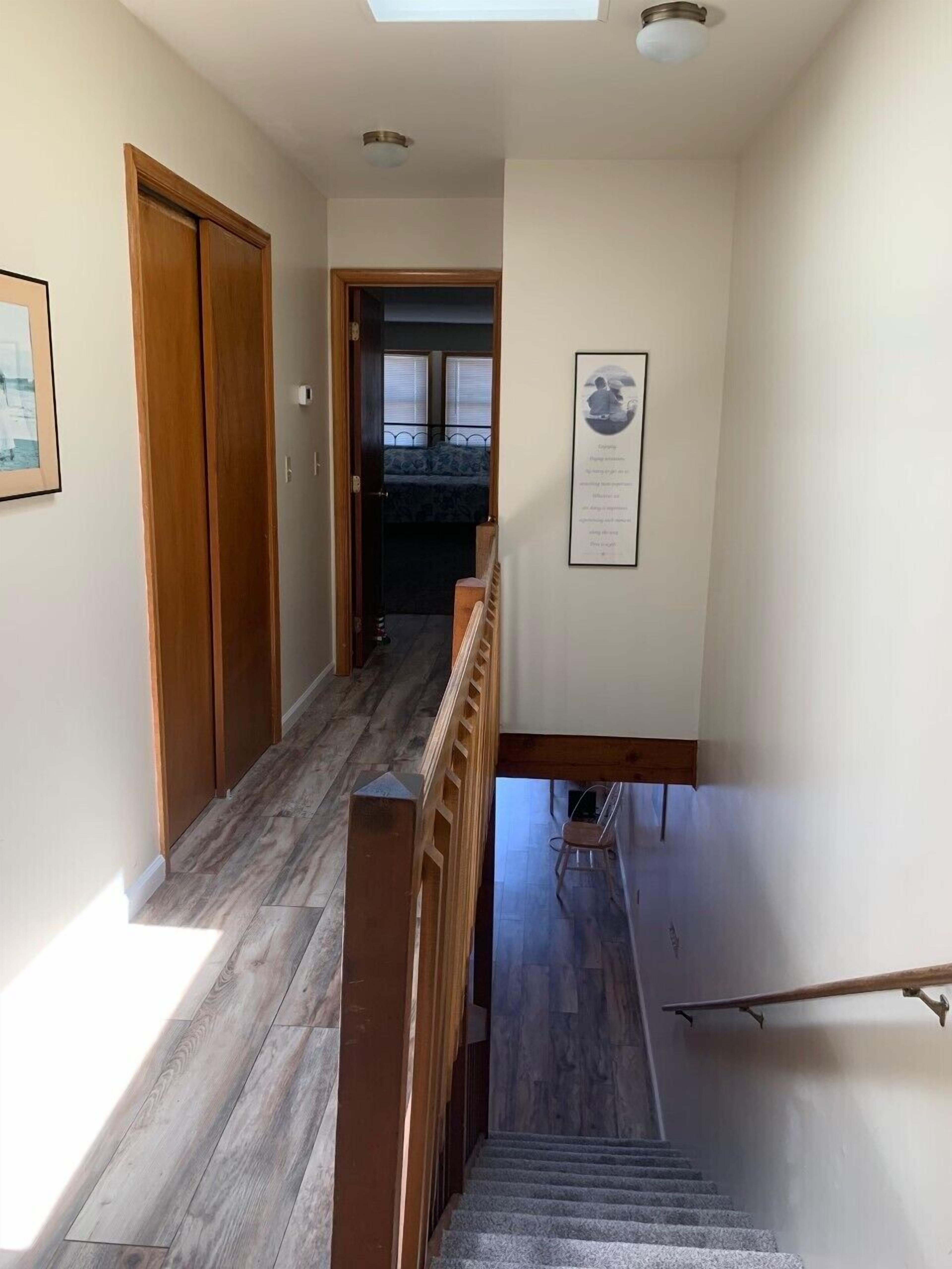 Un pasillo con suelo de madera, una escalera con barandilla de madera y una puerta que da a una habitación con cama.