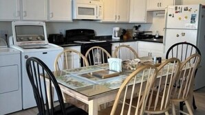 A compact kitchen with white cabinets, a microwave, a stove, and a refrigerator. There is a dining table with chairs. - Ocean view from the balcony of this 3 bedroom condo on 85th Street. (Ocean City)