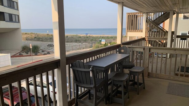 A covered outdoor area with a table and chairs, overlooking a beach and a parking lot. - Ocean view from the balcony of this 3 bedroom condo on 85th Street. (Ocean City)