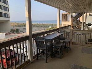 Un'area esterna coperta con tavolo e sedie, affacciata su una spiaggia e un parcheggio.