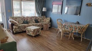 Una sala de estar con un sofá floral, un reposapiés a juego, una mesa de comedor de madera con mantel colorido y una silla de mimbre.