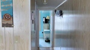 Un pasillo con suelo y paredes de madera que conduce a un baño con lavamanos y espejo.
