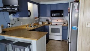 Una cocina con armarios azules, encimera de madera, estufa, microondas y refrigerador.
