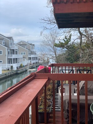 A wooden deck with a railing, overlooking a canal with houses in the background.