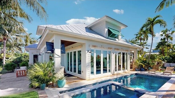 Une maison moderne avec une piscine, entourée de palmiers et d’une pelouse bien entretenue.