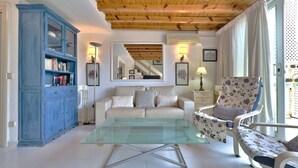 A living room with a glass coffee table, a sofa, a floral armchair, a blue cabinet, and a staircase in the background. - Skol 212. Two Bedrooms Duplex in Marbella Centre on the Beachfront. (Marbella)