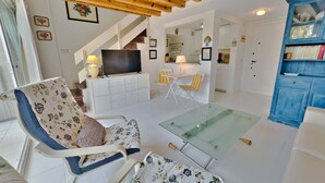 A living room with a sofa, a glass coffee table, a TV on a white cabinet, and a staircase leading to a kitchen. - Skol 212. Two Bedrooms Duplex in Marbella Centre on the Beachfront. (Marbella)
